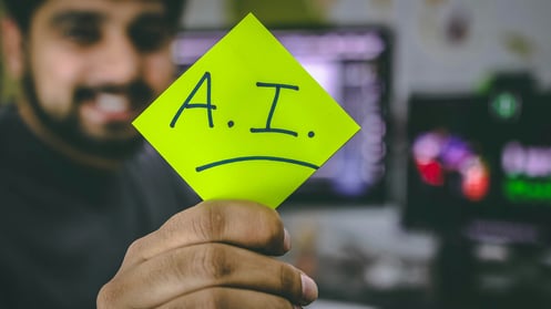 A man holds a posted note with the letters AI written on it.